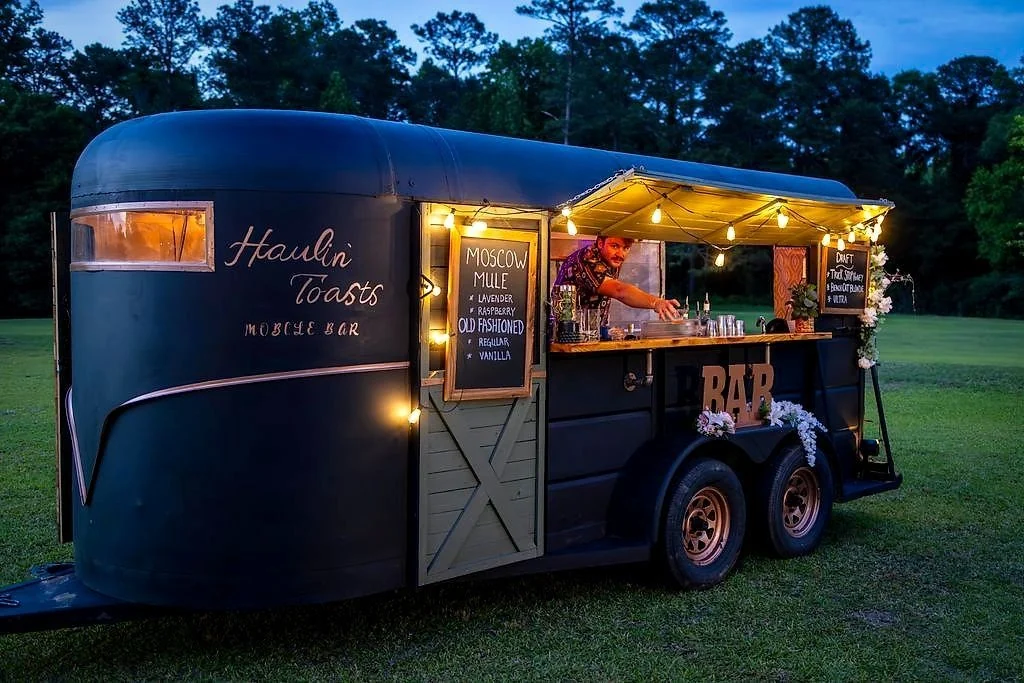 The Haulin’ Toasts mobile bar at dusk, hand-lettered and strung with lights